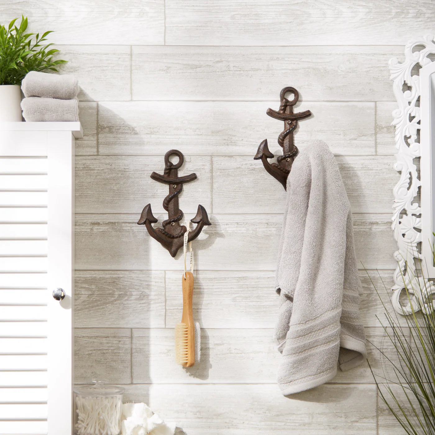 Cast iron anchor wall hooks holding a towel and bath brush on a tiled bathroom wall.