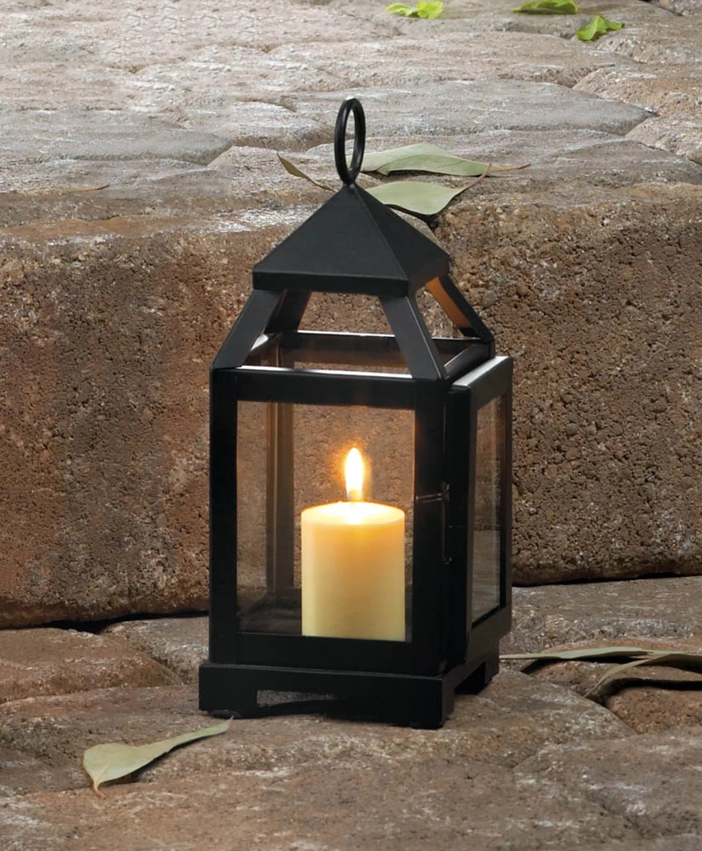 Black lantern with a lit candle on a stone surface