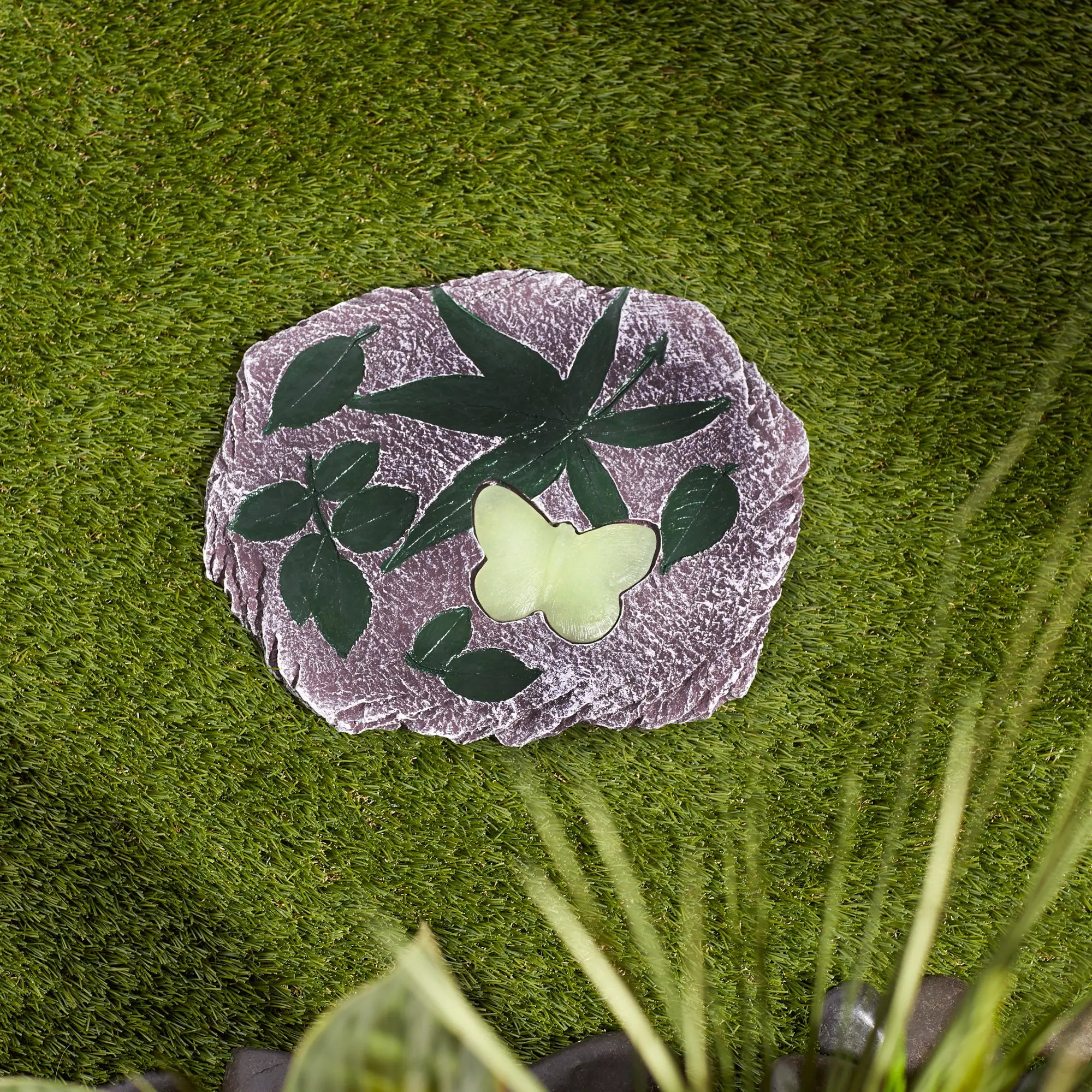 Garden stepping stone with butterfly and leaf design on a grassy background