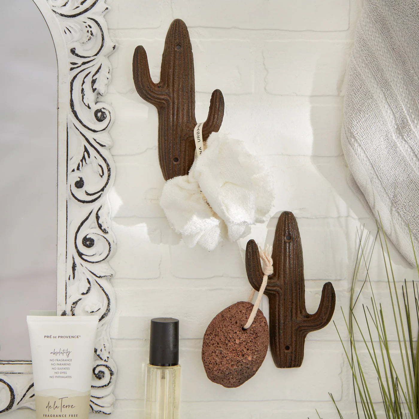 Set of 2 cast iron cactus wall hooks holding a bath sponge and washcloth on a bathroom wall.