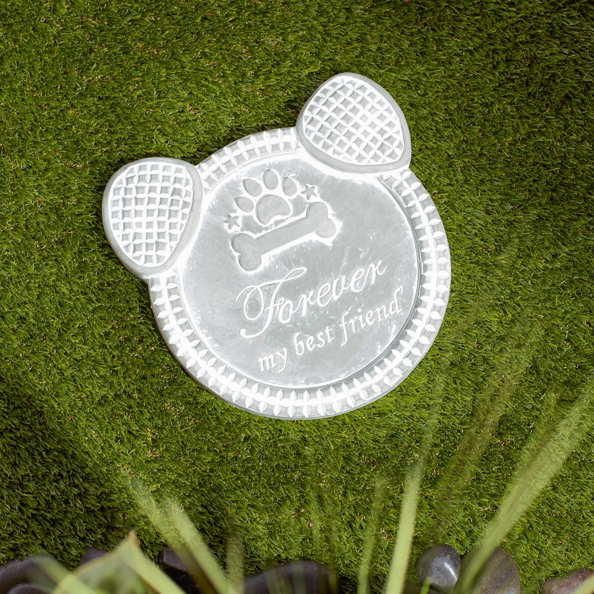 Paw-shaped dog memorial cement stepping stone with engraved text on grass