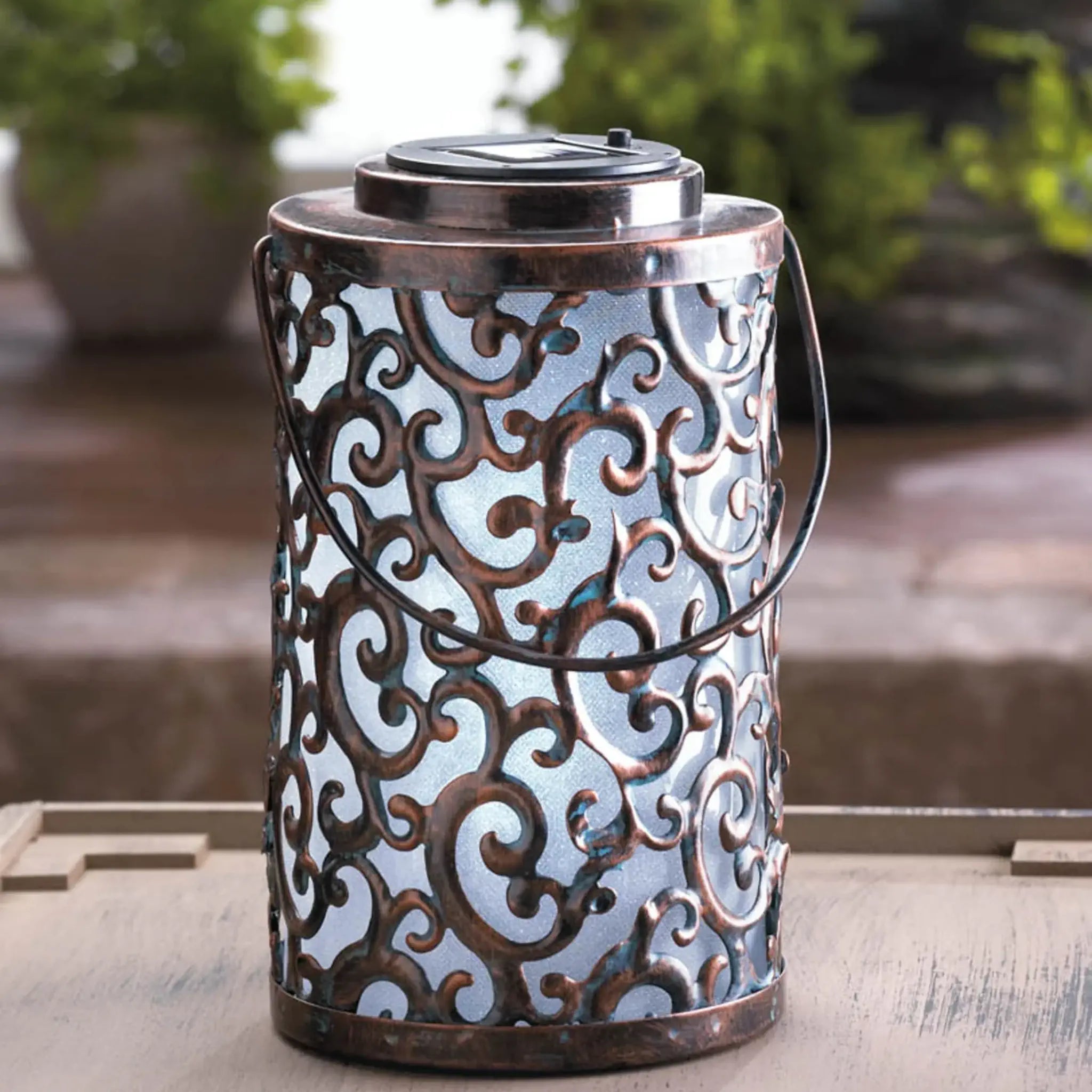 Decorative metal solar lantern with intricate patterns on a wooden surface.