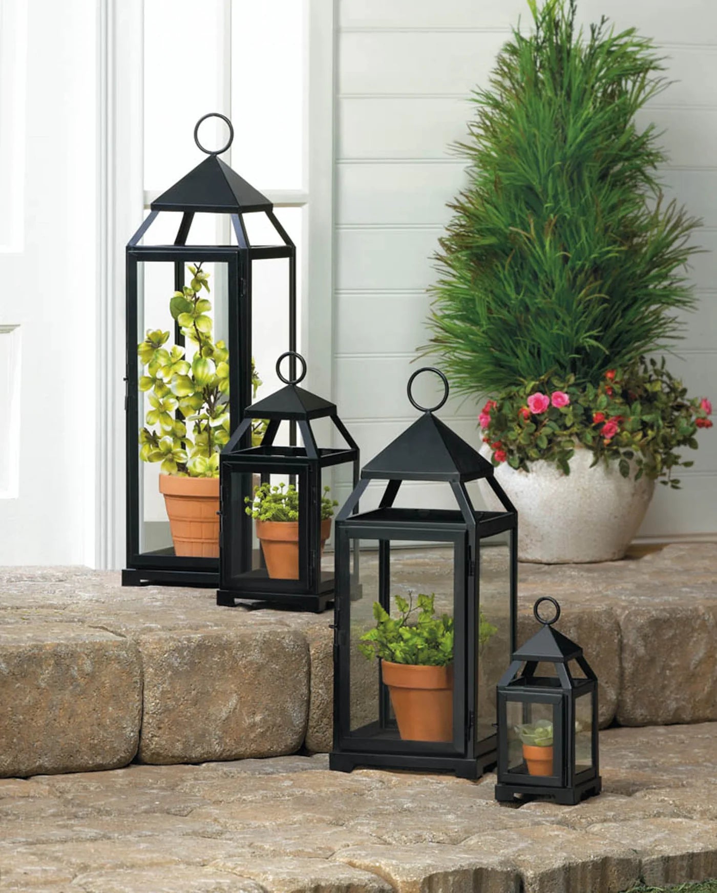 Set of black lanterns on a stone ledge with potted plants.