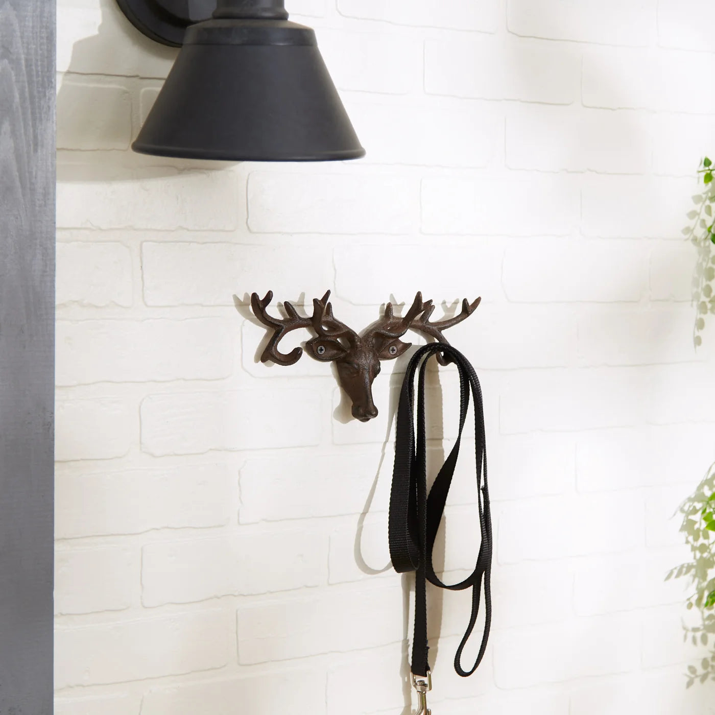 Decorative deer head wall hook with a black strap on a white brick wall.