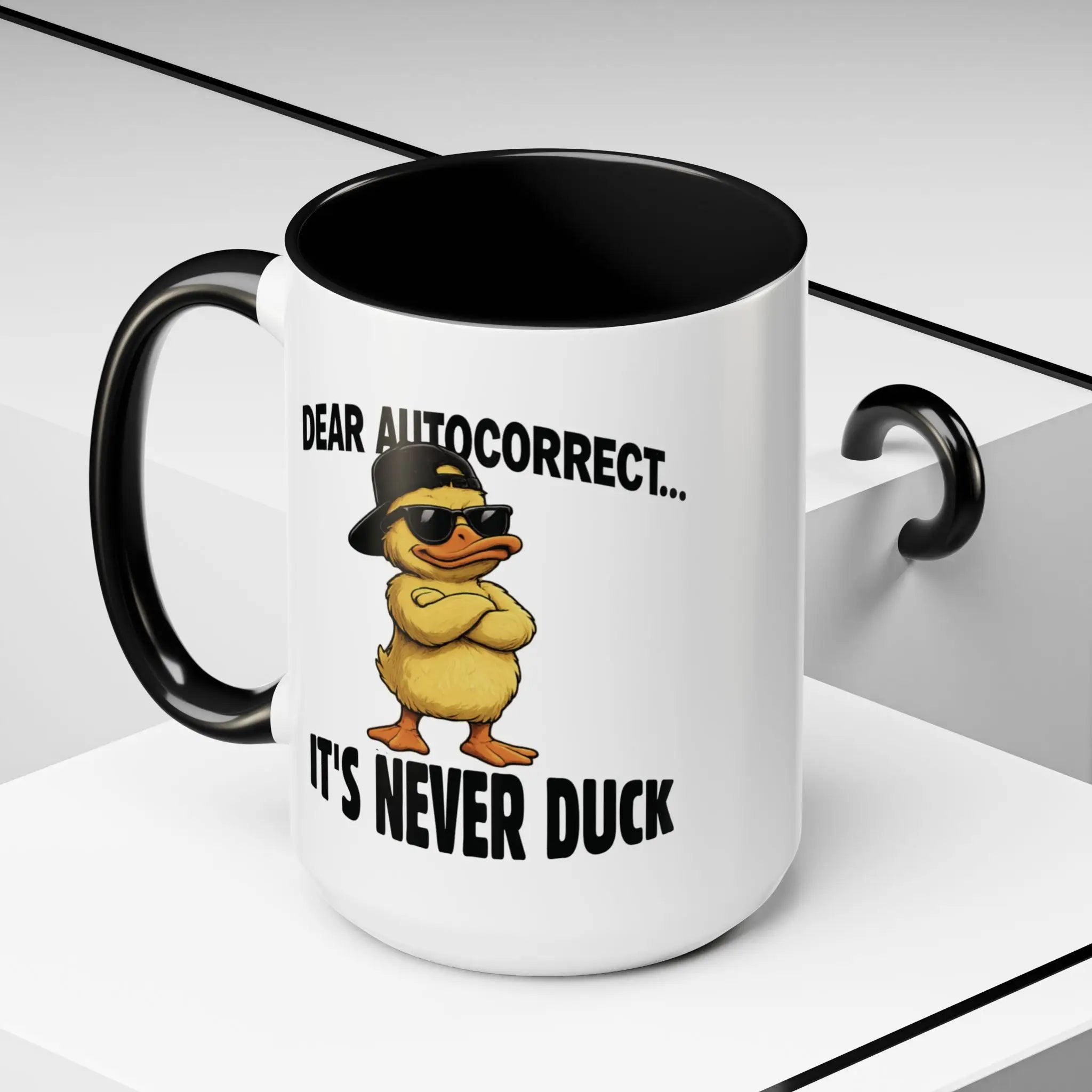Angled view of a white ceramic mug with black handle, duck design, and "Dear Autocorrect... It's Never Duck."