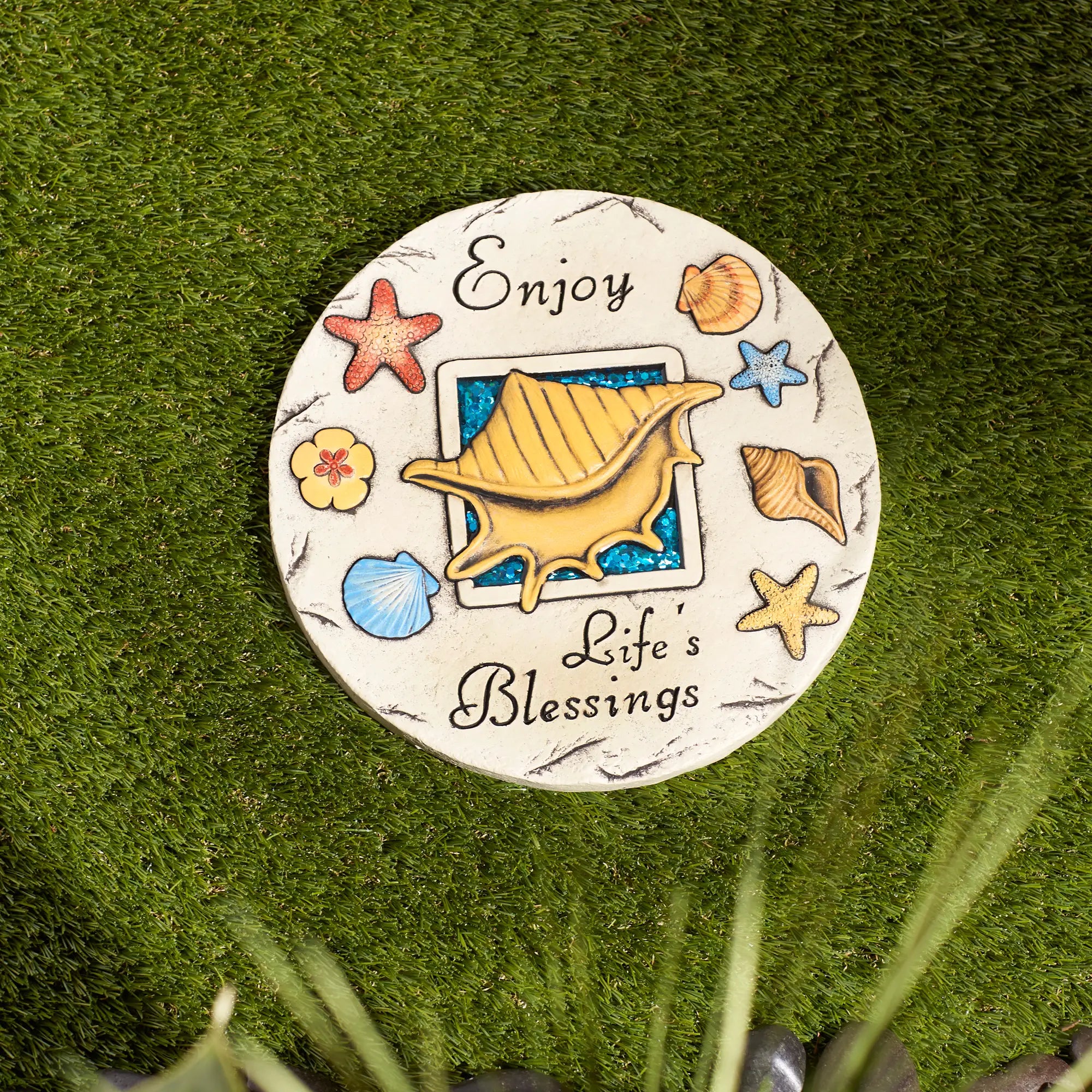 Garden stepping stone with shell design and 'Enjoy Life's Blessings' text on a grassy background