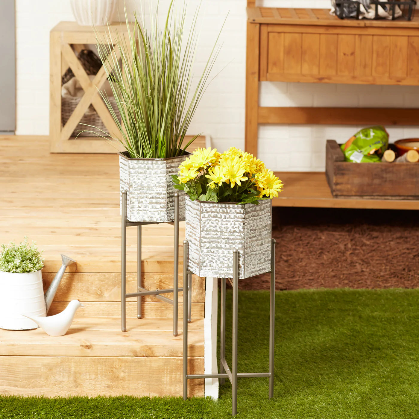 Two metal plant stands with decorative pots containing plants and flowers on a grassy area.