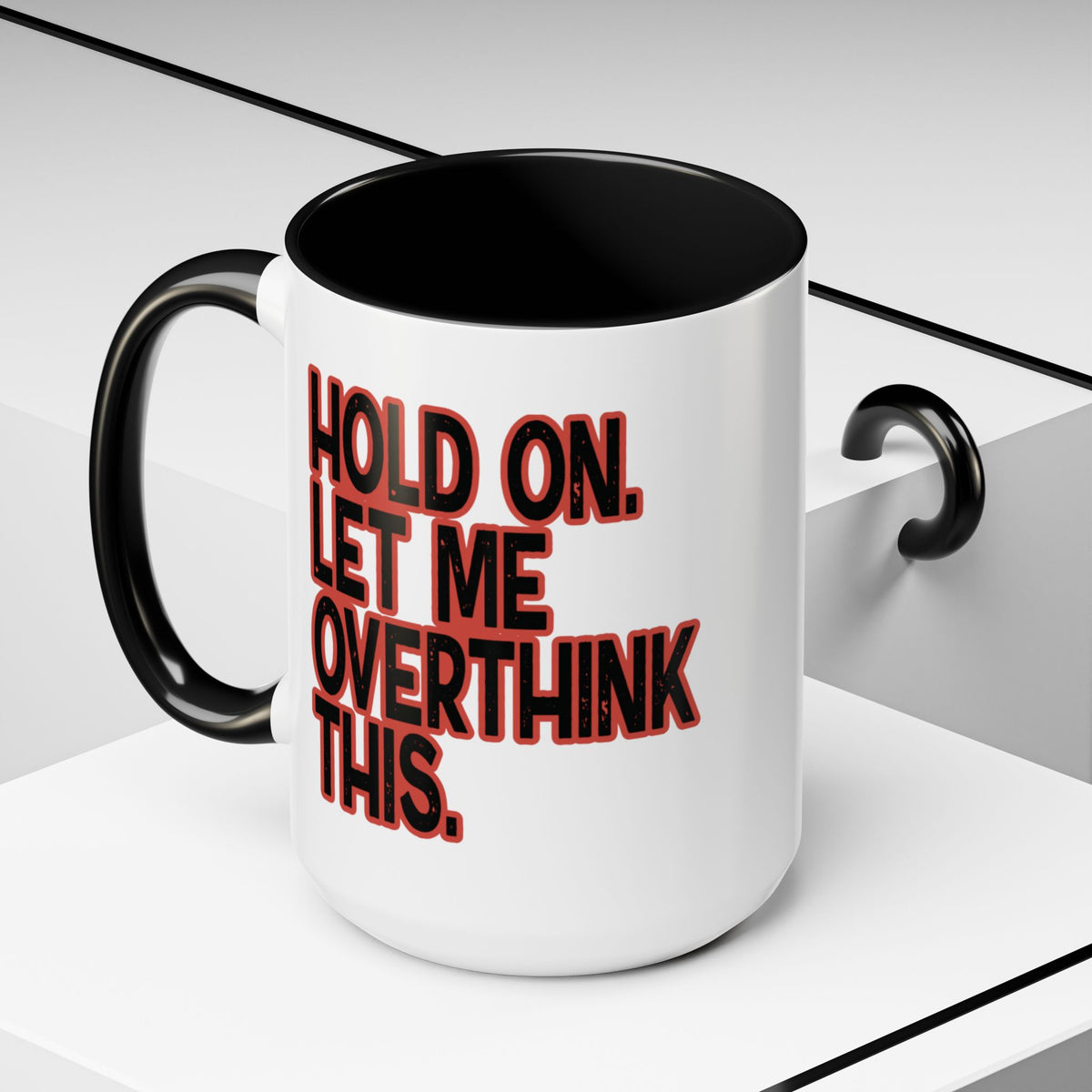 White 15 oz coffee mug on a geometric display with “Hold On. Let Me Overthink This” in distressed black lettering outlined in red.