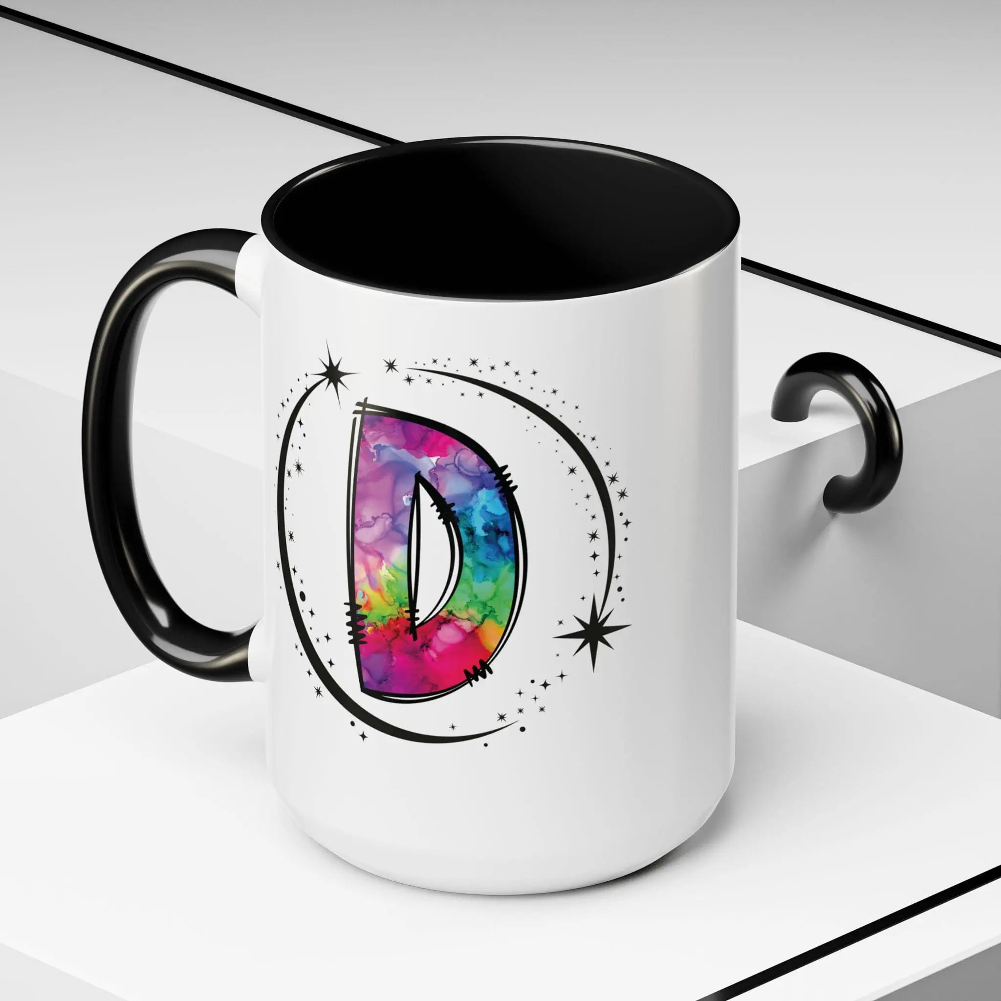 White monogram mug with black handle and interior featuring a colorful letter D design on decorative background