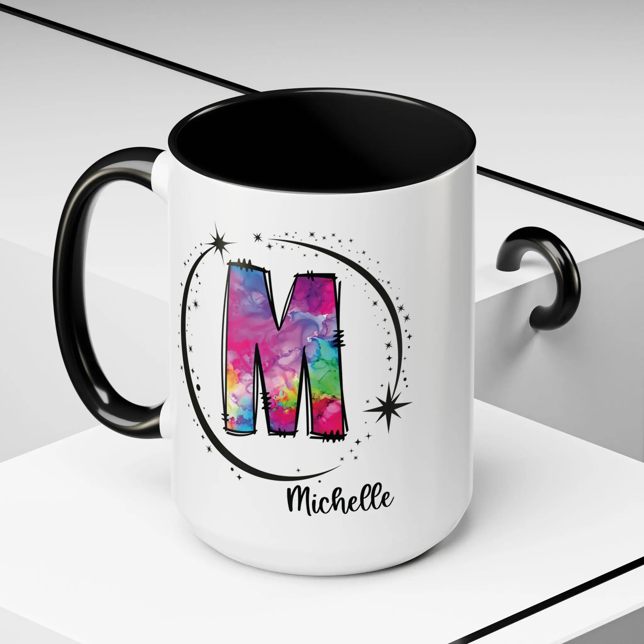 White monogram mug with black handle and interior featuring a colorful letter M design and custom name on decorative background