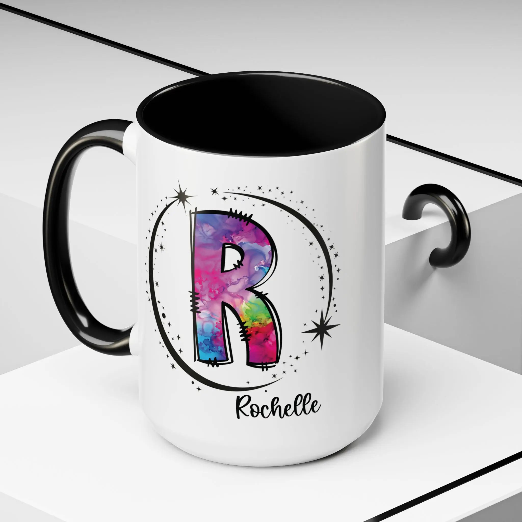 White monogram mug with black handle and interior featuring a colorful letter R design and custom name on decorative background