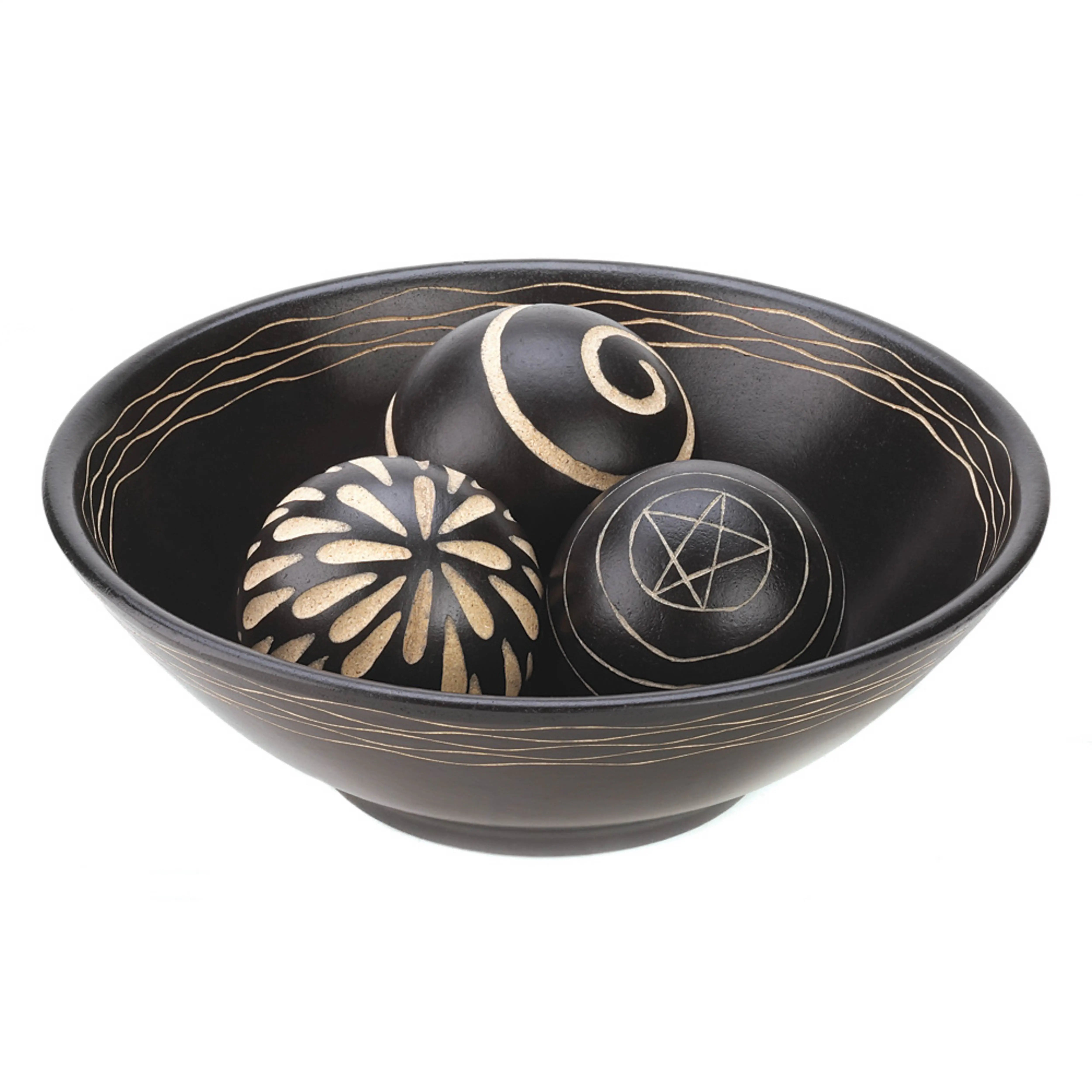 Black bowl with gold decorative elements containing three black balls with gold patterns on a white background
