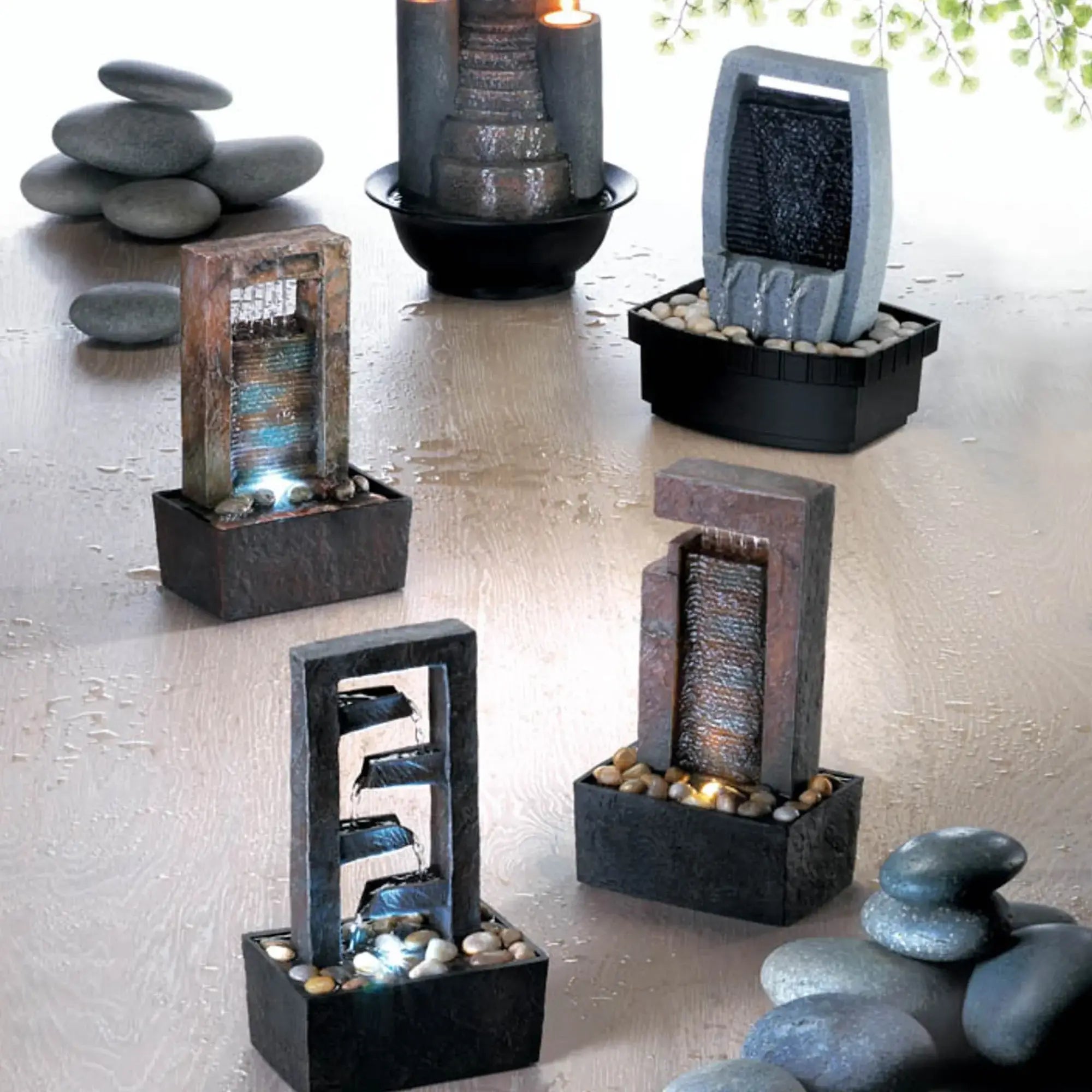 Set of small tabletop fountains with rocks and lights on a light surface.